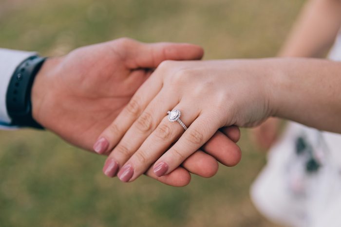 Finances In Marriage Blog Header Of Groom Holding Brides Hand With Oval Engagement Ring