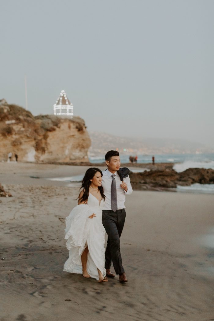 Groom Walking with Bride at Laguna Beach Wedding While Bride is Wearing Unique Casual Wedding Dress Elsie by Rebecca Ingram