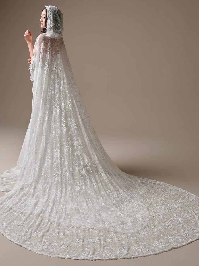 Bride wearing Maggie Sottero Bellevue lace cape accessory , a sheer lace bridal cape with hood and long train layered over a strapless lace wedding dress, shown in close-up and full back view