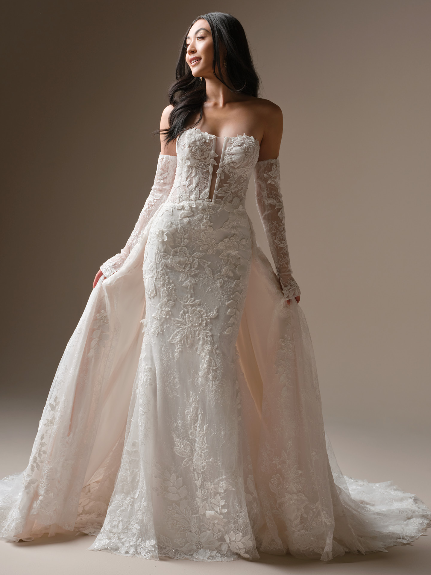 Bride wearing Maggie Sottero Laurie train detachable lace train with long sleeves over a strapless lace wedding dress, full-length view with dramatic train.