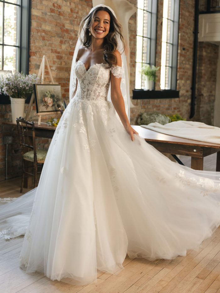 Verina ballgown wedding dress with off the shoulder lace sleeves, a floral lace bodice, layered tulle skirt, and cathedral veil styled in a bright loft studio.