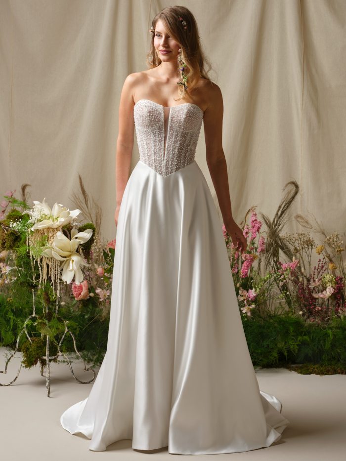 Marty A-line wedding dress featuring a strapless beaded bodice with pearl like texture and a clean satin skirt styled in a floral studio setting.