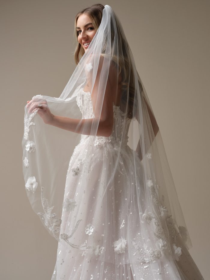 Bride wearing Sottero and Midgley Athlone A-line wedding dress with floral appliqué paired with a fingertip veil with floral lace appliqué, side view.