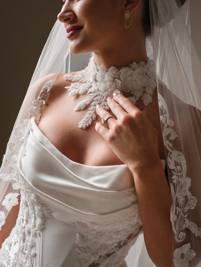 Bride wearing Sottero and Midgley Burke choker accessory with floral lace detailing, styled with a strapless draped wedding dress and lace-edged veil, close-up view.