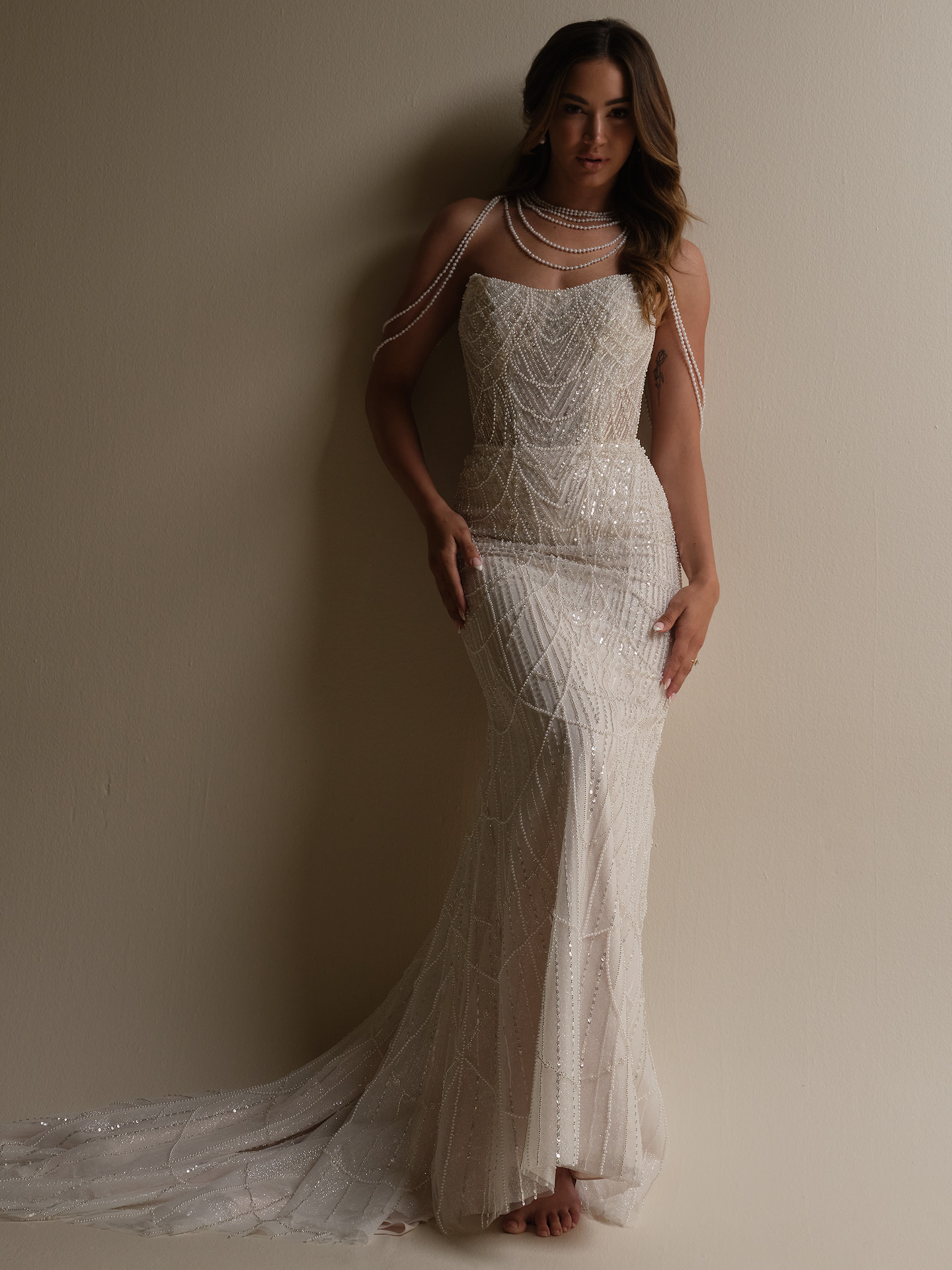 Bride wearing Sottero and Midgley Constance sheath wedding dress with pearl draped shoulder accessory, featuring a strapless beaded wedding dress with layered pearl strands draped over the shoulders and neckline.
