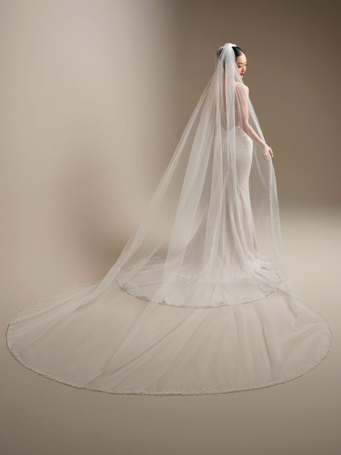 Sottero and Midgley Cooper cathedral veil with pearl edge extending into a long train, shown from the back with a pearl beaded fit-and-flare wedding dress.
