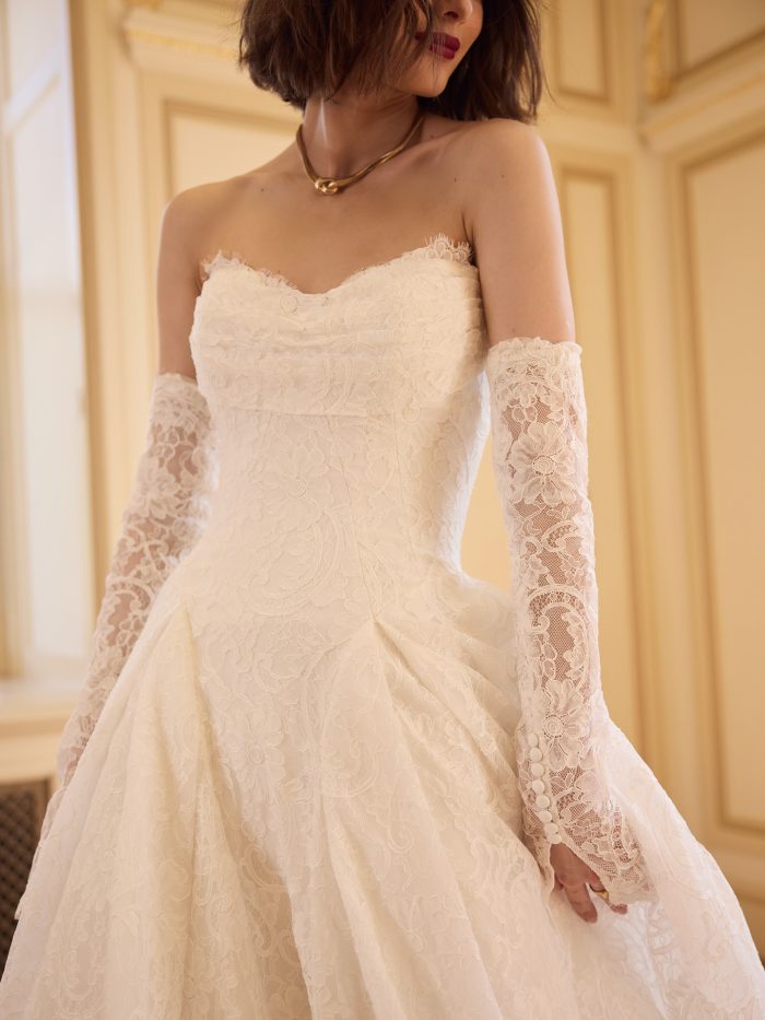 Tamar A-line wedding dress with a strapless lace bodice, detachable lace sleeves, and a voluminous lace skirt shown in a close up studio shot.