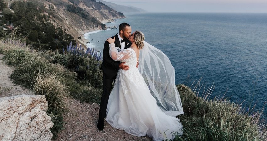 Bride wearing a long sleeve wedding dress by Maggie Sottero hugging her husband on a seaside cliff