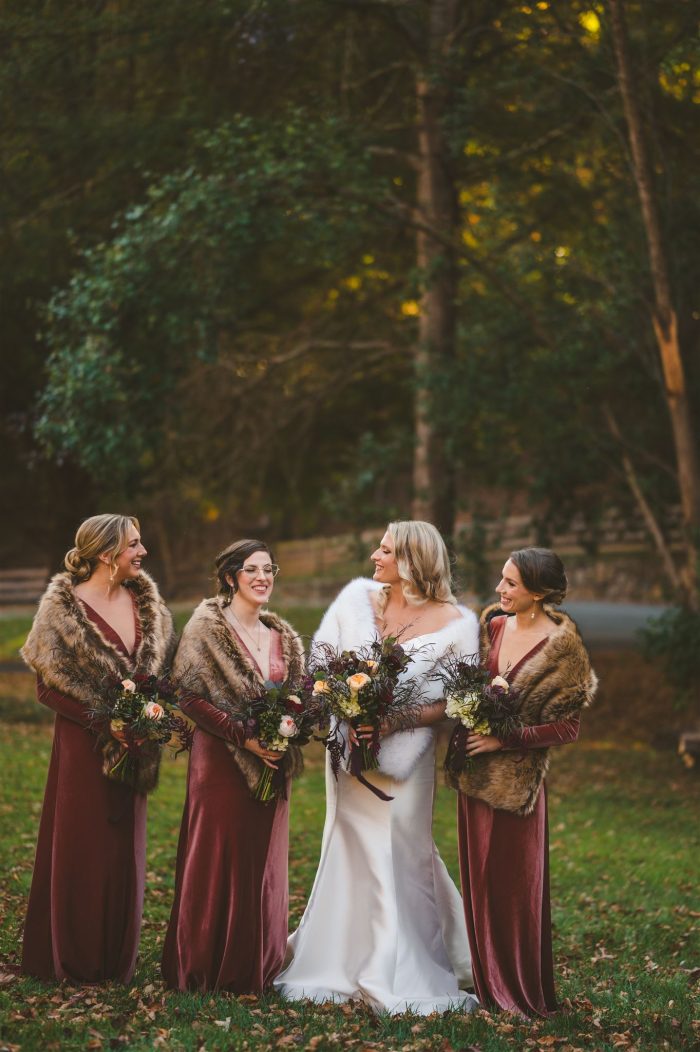 Bride In Satin Winter Wedding Dress Called Josie By Rebecca Ingram With Fur Wrap And Bridesmaids In Red Bridesmaids Dresses