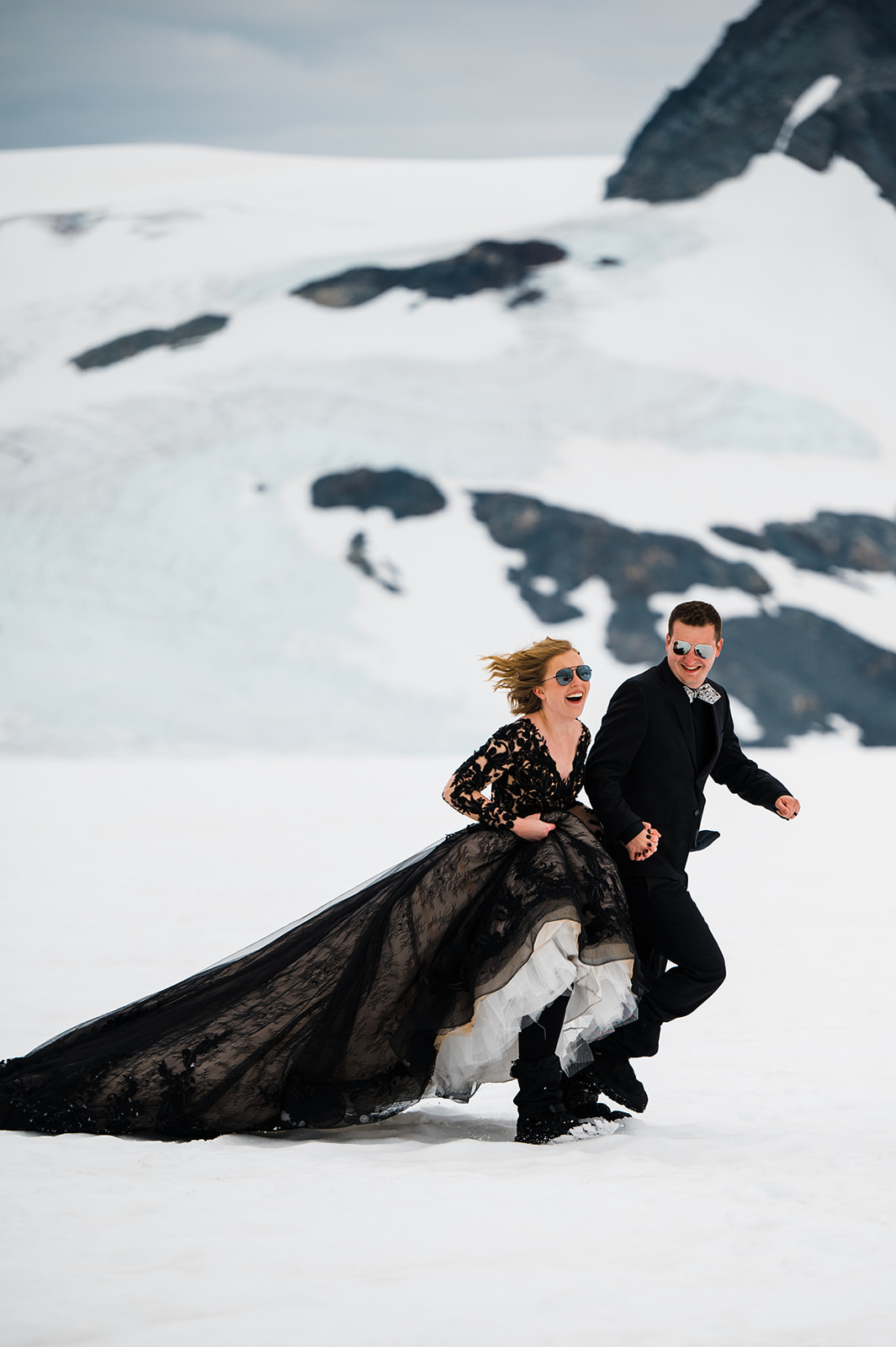 Mariée exhibant sa robe dans la neige avec le marié dans une robe appelée Zander par Midgley et Sottero