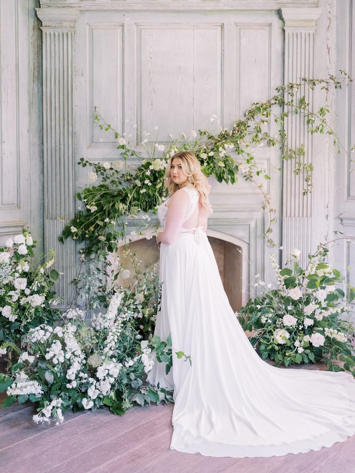 Bride By Flowers And Fireplace Wearing A Dress Called Gabriella By Rebecca Ingram 