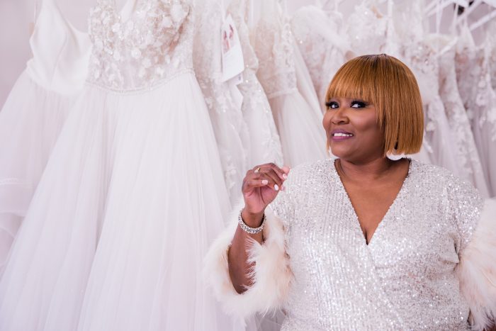 Black Owned Businesses Owner LaTonya Turnage Of Elite Secrets Bridal Standing In Front Of Maggie Sottero Wedding Gowns