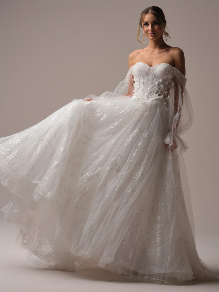 Bride wearing the Ireland A-line wedding dress by Maggie Sottero, featuring a strapless sweetheart neckline, pleated illusion bodice with exposed boning, and a flowing glitter tulle skirt with soft sparkle and an extended illusion train.