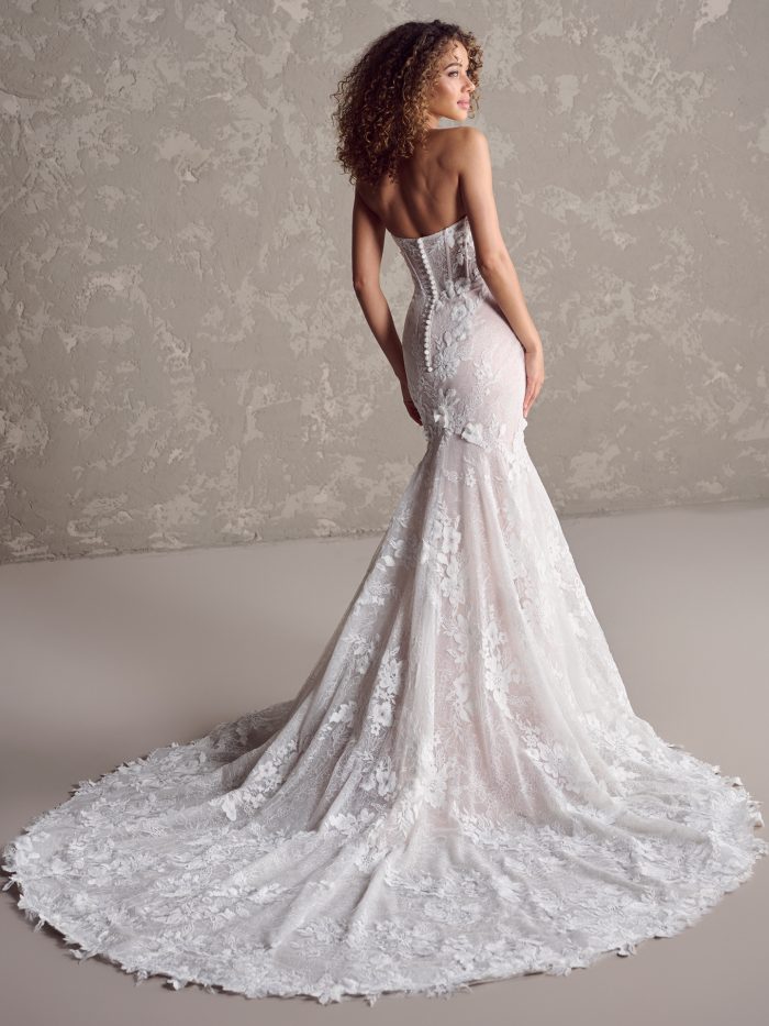 Back view of the Ortensia wedding dress showing the fitted lace silhouette, covered button closure, and long lace train with floral detailing.