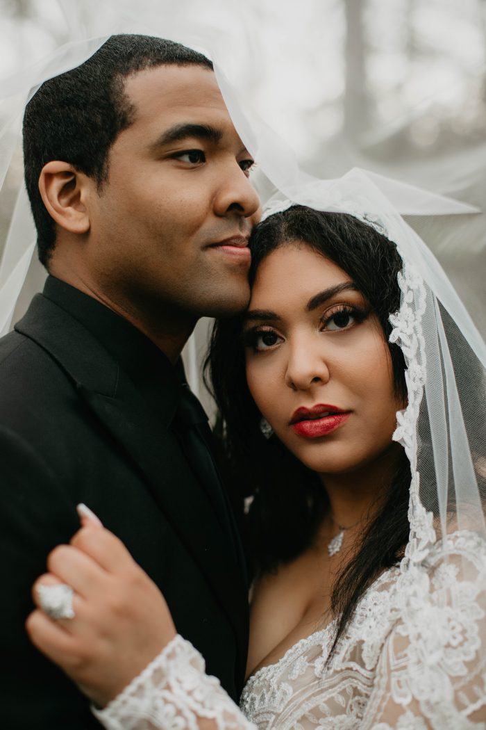 Black Bride Standing With Husband Under Clear Umbrellas Wearing An A-Line Lacy Wedding Gown Called Mallory Dawn By Maggie Sottero