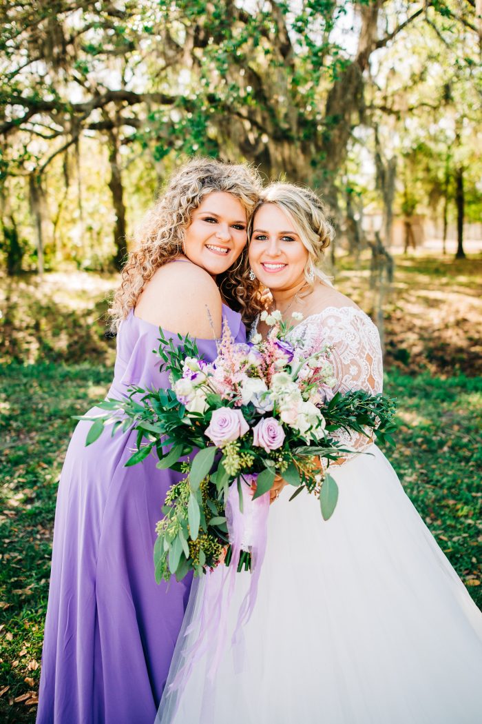 Bride Standing With Bridesmaid Wearing Purple Wearing A Bridal Dress Called Mallory Dawn By Maggie Sottero