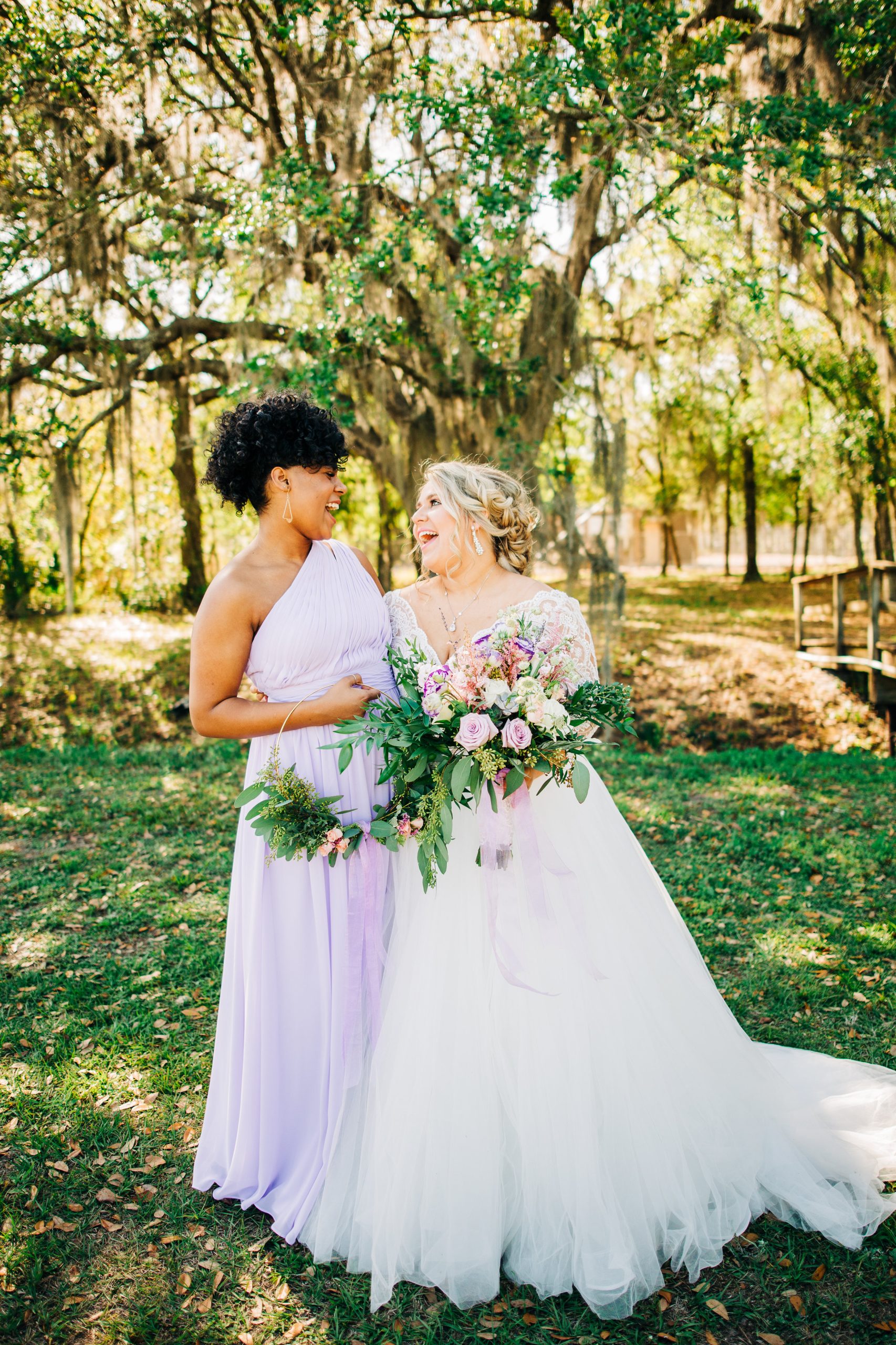 Mariée debout avec une demoiselle d'honneur vêtue de violet vêtue d'une robe de mariée appelée Mallory Dawn par Maggie Sottero