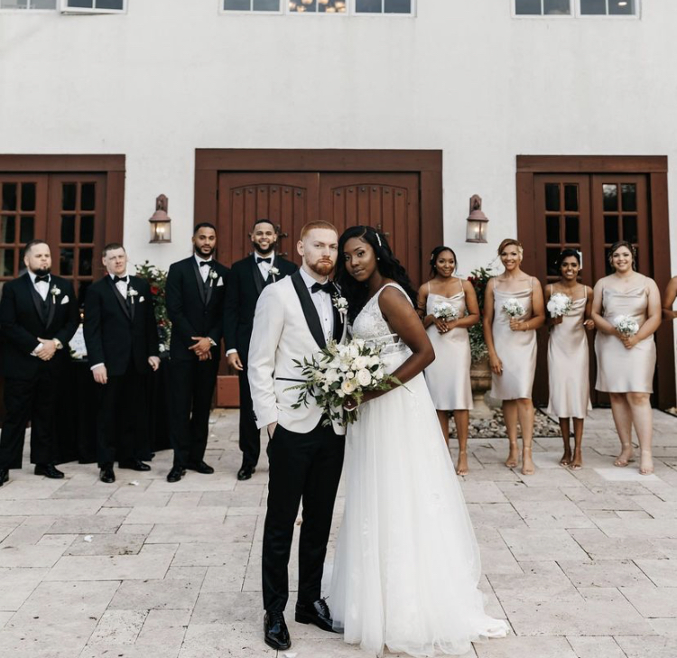 La mariée porte une robe de mariée abordable appelée Raelynn par Rebecca Ingram avec une soirée nuptiale en or et noir
