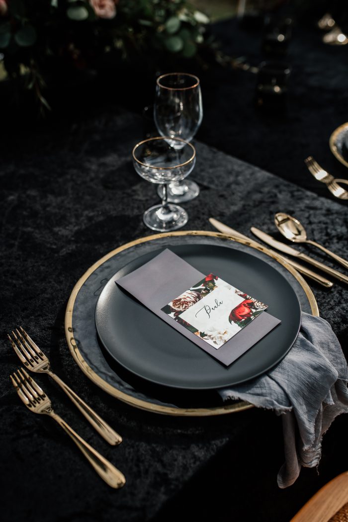 Wedding Reception Place Setting Of Black Plate, Golden Silverware, And Red Placecard