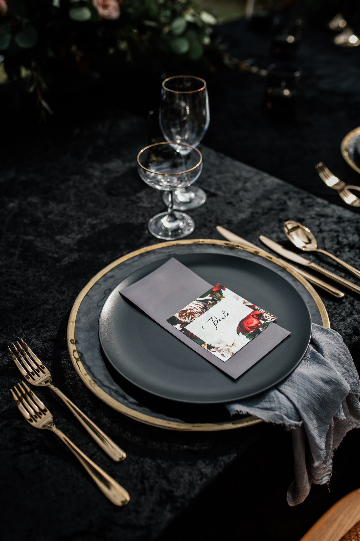 Lieu de réception de mariage avec assiette noire, argenterie dorée et marque-place rouge