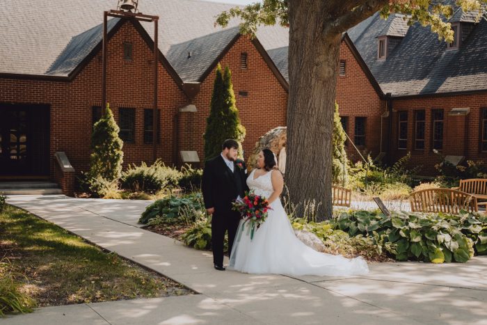 Bride Wearing Glamorous Ballgown Called Taylor Lynette By Maggie Sottero Standing In Front Of Church With Groom