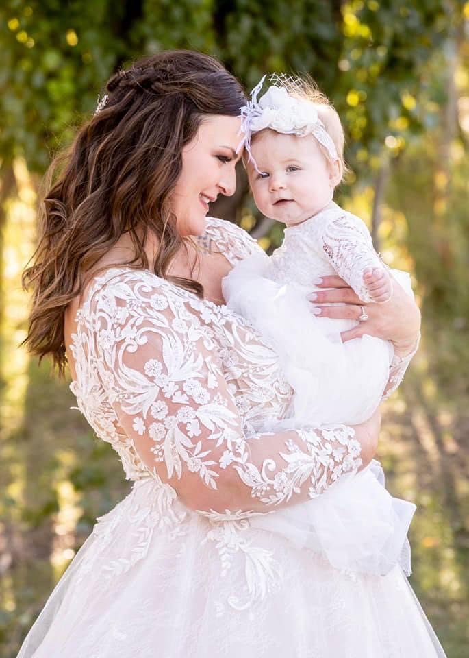 Curvy Bride In Long Sleeved A-Line Wedding Gown Called Zander By Sottero And Midgley Holding Daughter