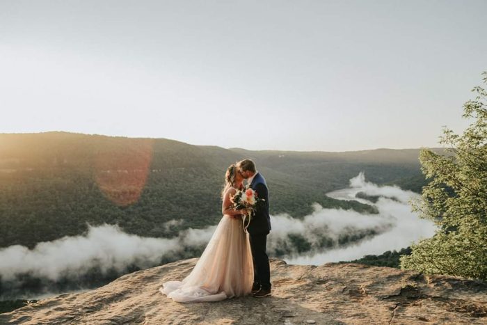 Weding Venue Ideas Of A Woodsy OUtdoor Wedding With Bride And Groom On Mountain Wearing A Dress Called Raelynn By Rebecca Ingram