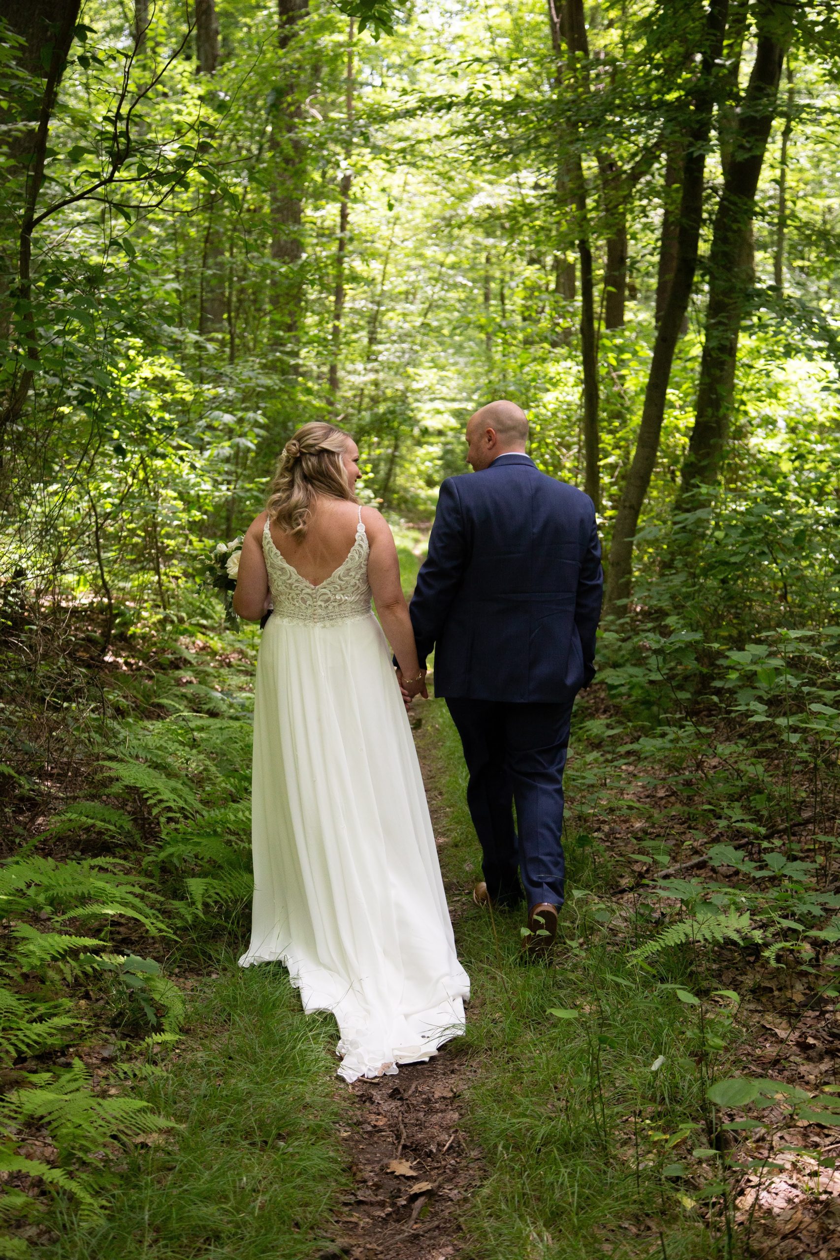 Mariée portant une robe de mariée de printemps appelée Lorraine par Maggie Sottero debout dans les bois avec le marié en robe de mousseline