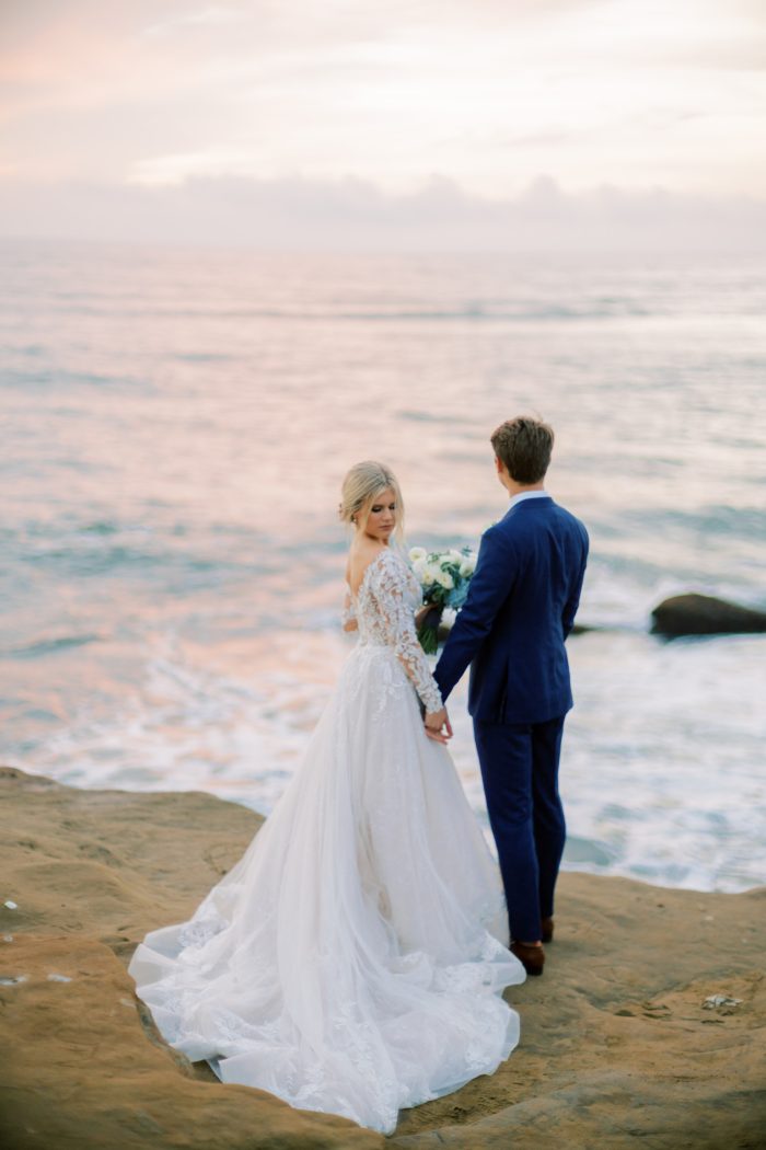 Bride Wearing Lace A-Line Wedding Dress With Sleeves Called Zander By Sottero And Midgley On Seaside Cliff With Groom