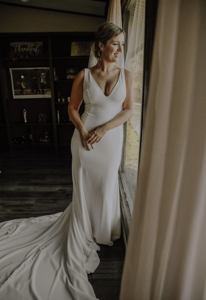 Bride Wearing Simple Crepe Wedding Gown Called Fernanda By Maggie Sottero Standing By Window