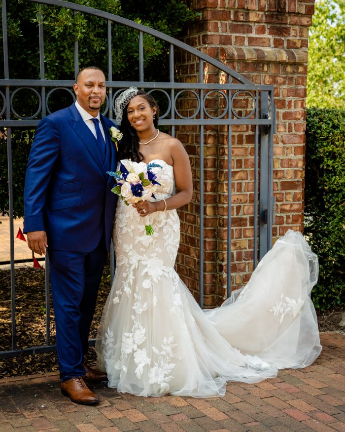 Bride Wearing Spring Wedding Dress With Groom In Navy Blue Suit Holding Bouquet Wearing A Gown Called Hattie By Rebecca Ingram