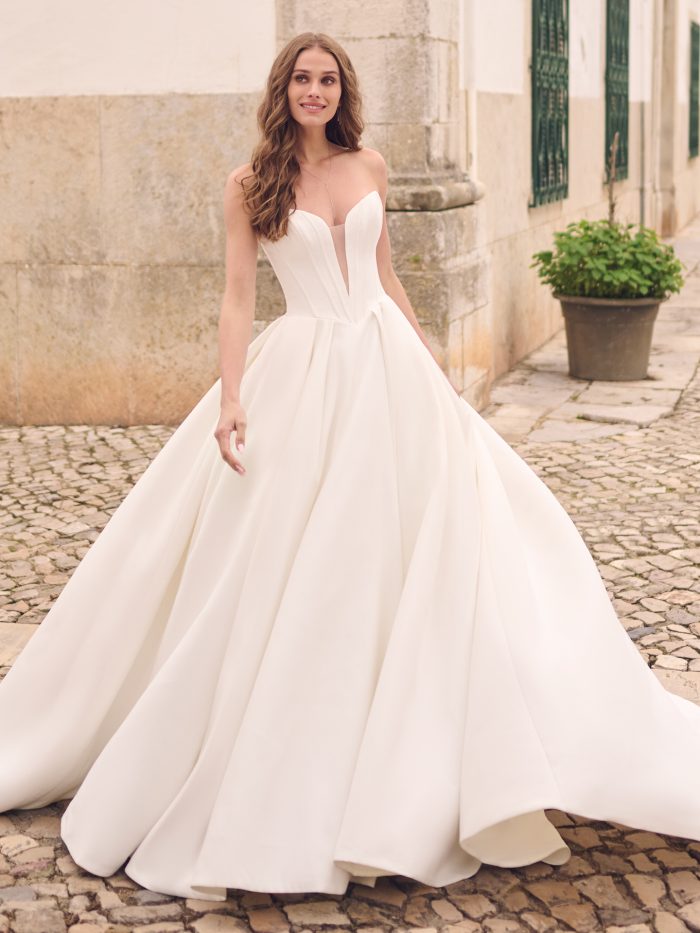 Derrick by Maggie Sottero — modern strapless ballgown wedding dress featuring a deep illusion plunge neckline, structured Mikado bodice, and full pleated skirt.