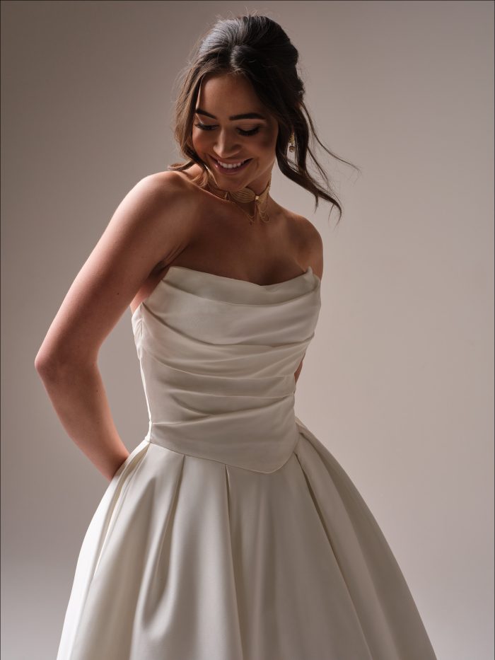 Close-up of Maureen by Maggie Sottero — elegant strapless satin ballgown with ruched bodice, cowl neckline, and chic pleated skirt.
