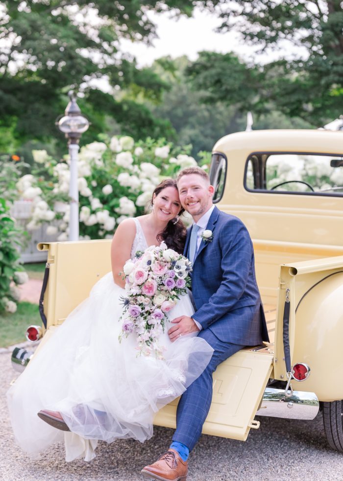 Bride Wearing Lace A-Line Wedding Dress Called Raelynn By Rebecca Ingram With Groom In Front Of Yellow Vintage Truck