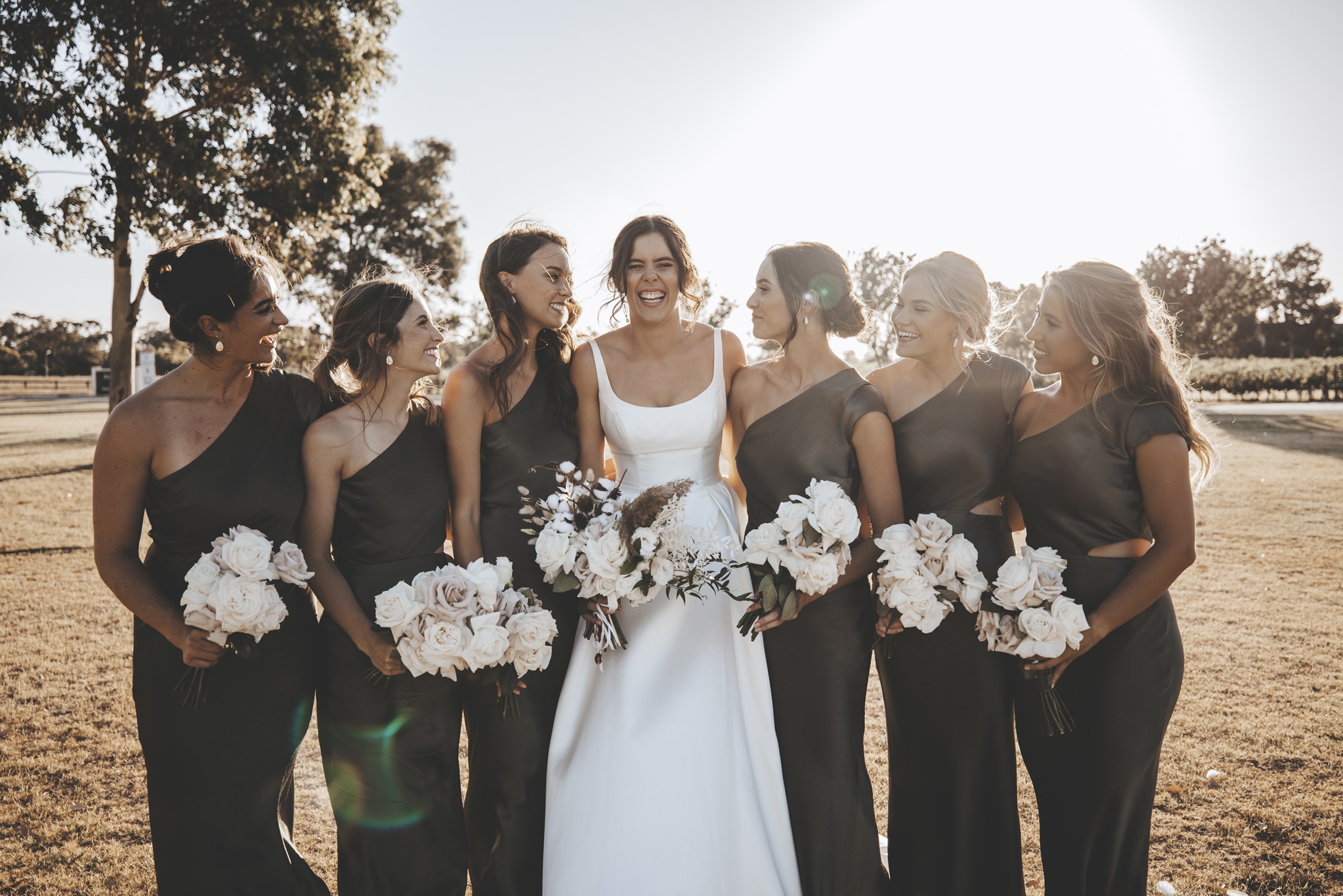 Mariée portant une robe de mariée en satin appelée Selena par Maggie Sottero debout avec des demoiselles d'honneur portant du vert Forrest