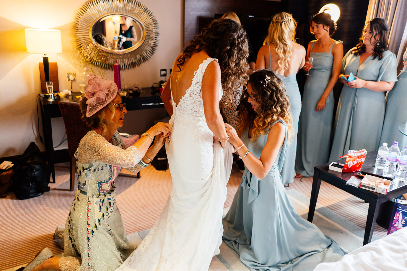 Mariée vêtue d'une robe de mariée en dentelle appelée Delilah, aidée par ses demoiselles d'honneur en bleu dans sa robe