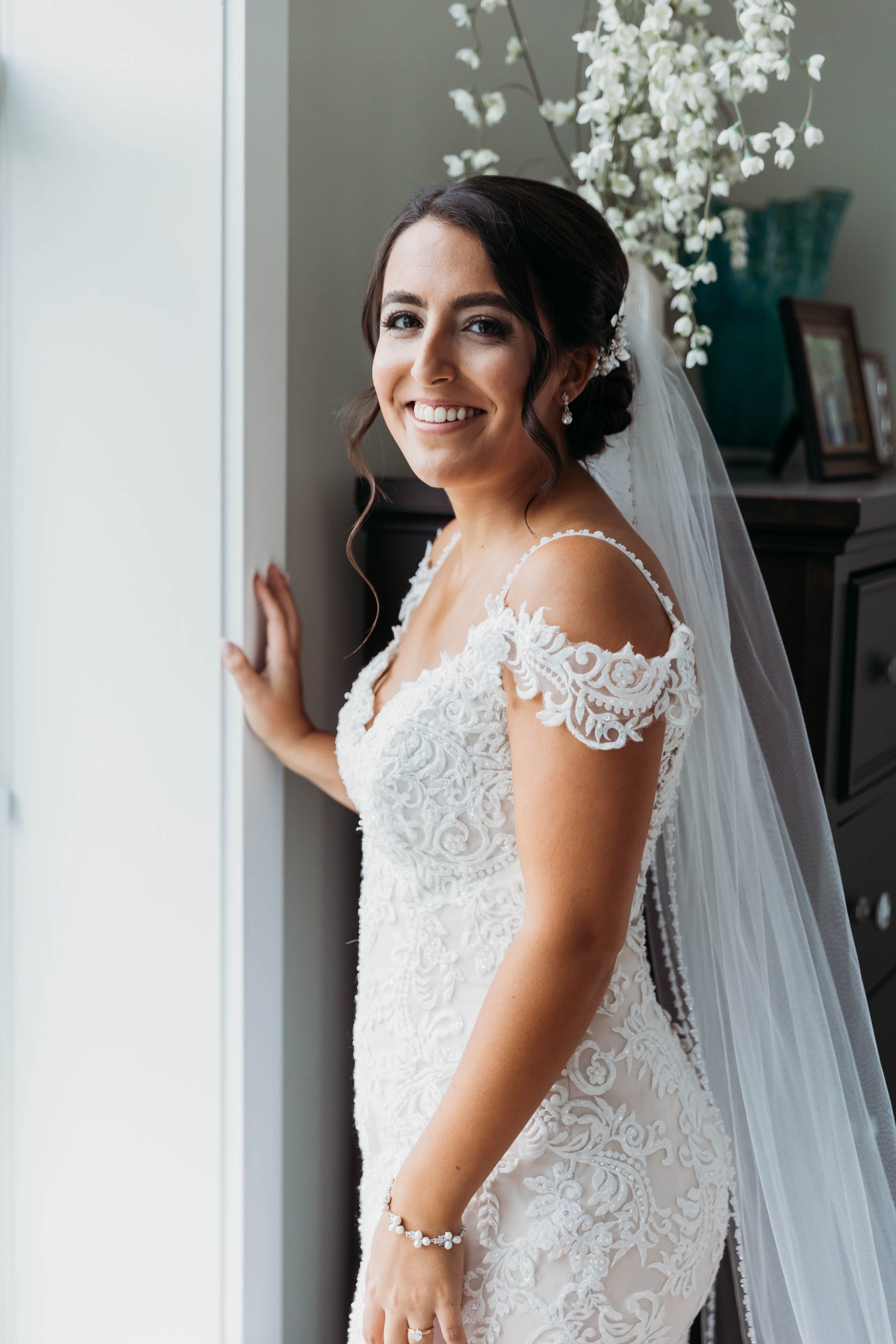 Mariée portant une robe de mariée en dentelle appelée Katell par Maggie Sottero devant la fenêtre