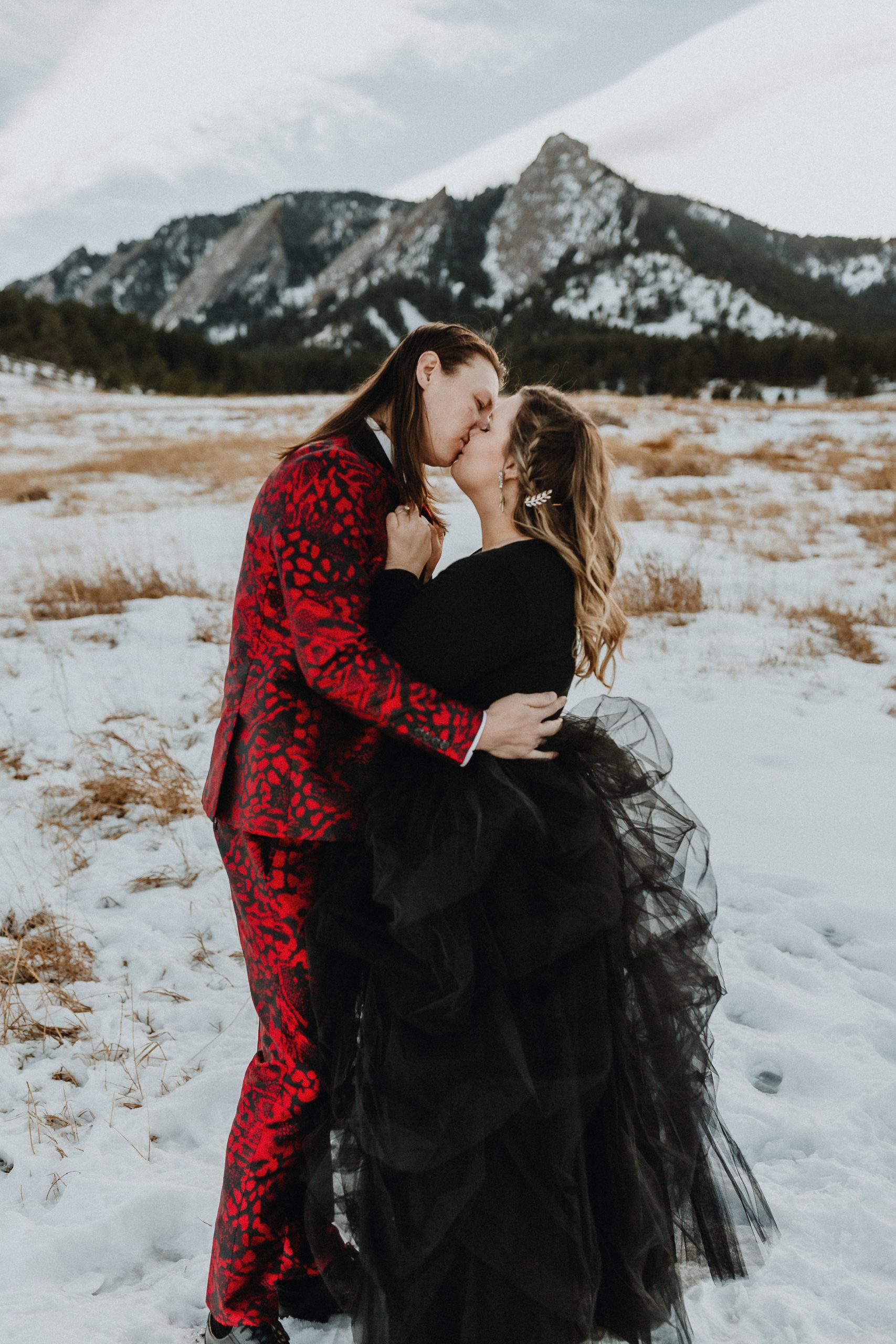 Mariée portant une robe noire avec un fiancé en costume rouge lors d'une séance photo de fiançailles dans les montagnes