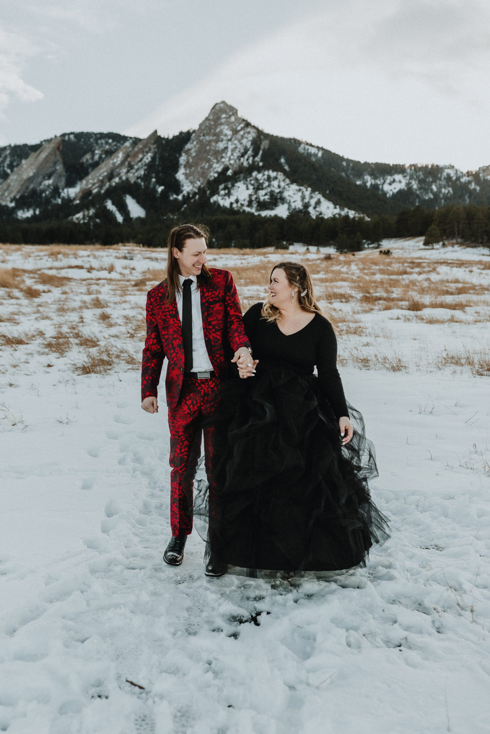 Mariée portant une robe noire avec un fiancé en costume rouge lors d'une séance photo de fiançailles dans les montagnes