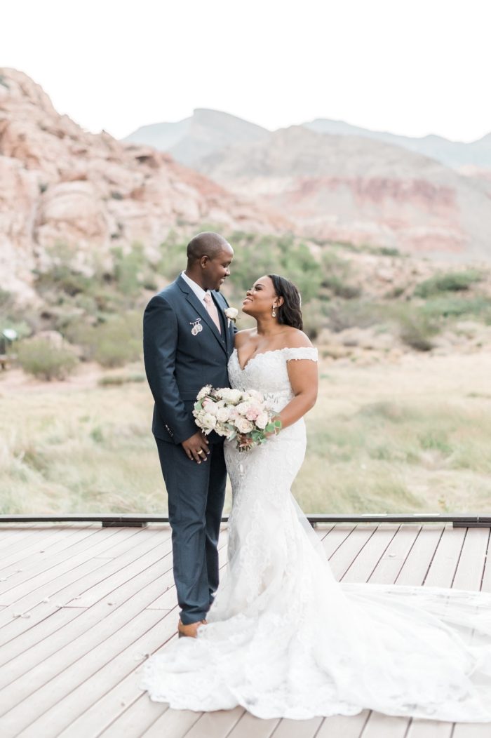 Bride Standing With Her Groom In Front Of Desert Rock Wearing A Fit-And-Flare Wedding Dress Called Kennedy By Maggie Sottero