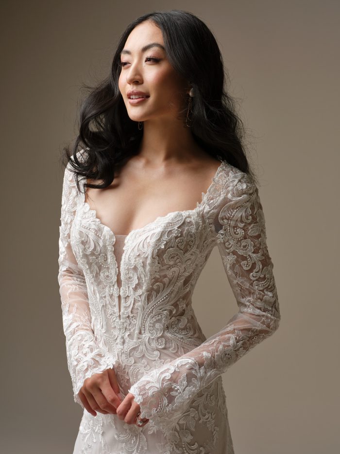 Close-up of the Farrah gown by Maggie Sottero, showcasing the deep sweetheart neckline, sheer lace long sleeves, and intricate embroidered lace bodice with corset detailing.
