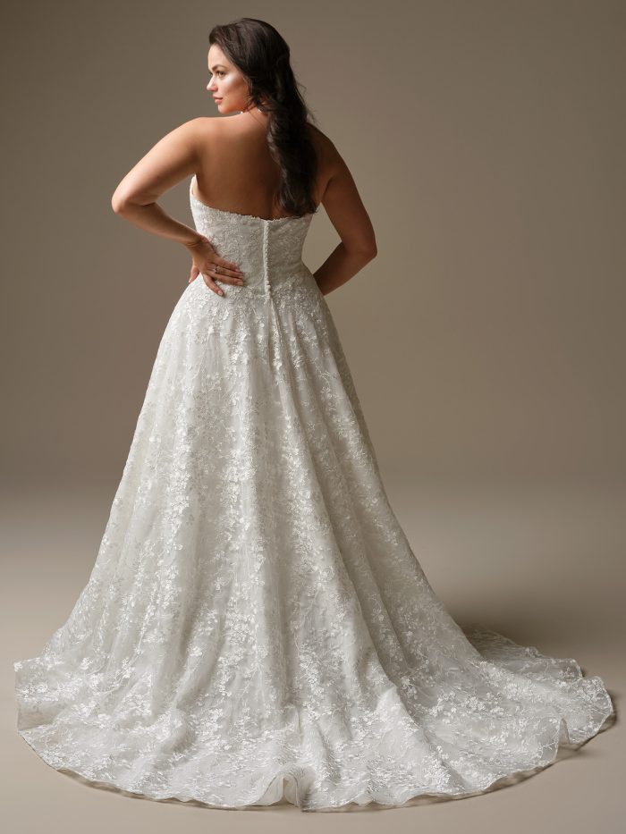 Back view of the Memphis ballgown wedding gown by Maggie Sottero, showcasing the strapless neckline, button-back closure, and full shimmering lace skirt with chapel-length train.