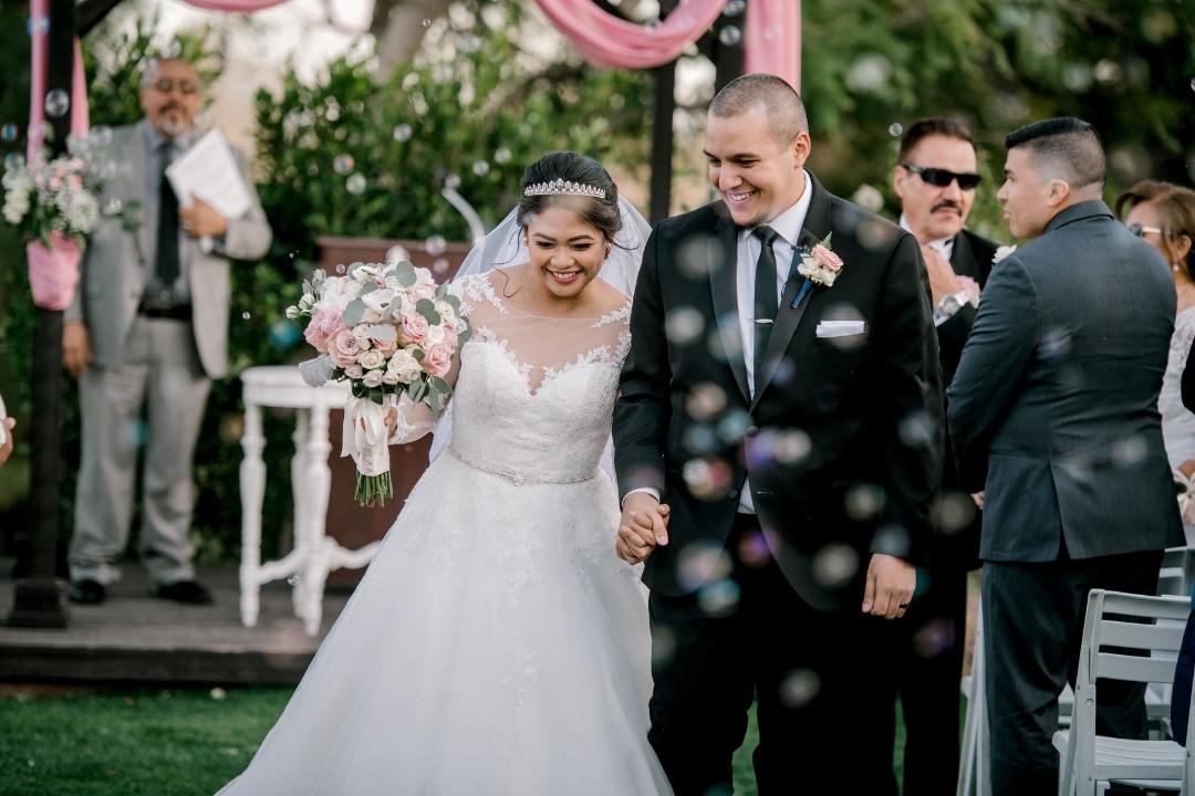 Mariée asiatique portant une robe de mariée en dentelle appelée Olivia par Rebecca Ingram avec des fleurs et un marié