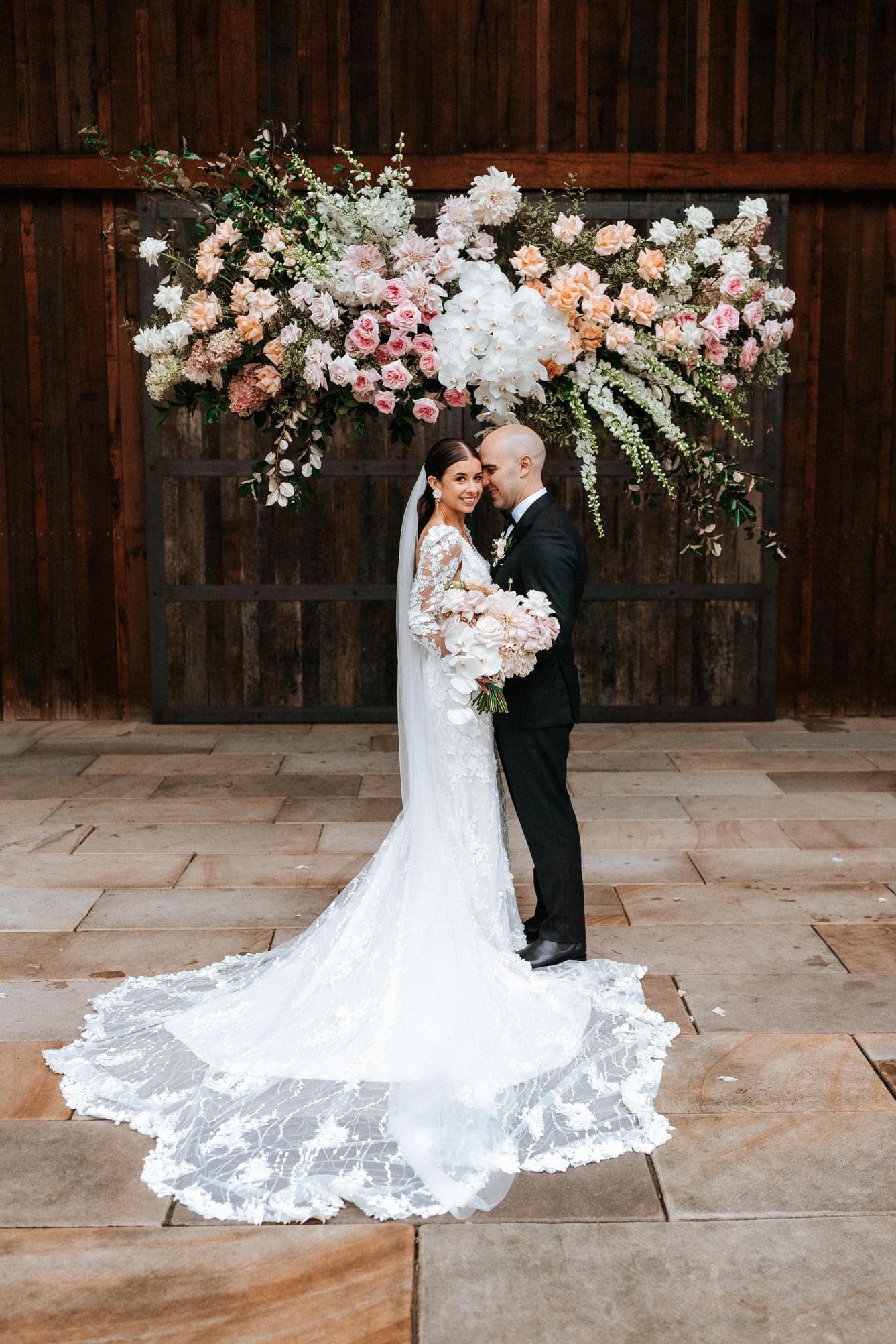 Mariée portant une robe de mariée d'été romantique à manches longues appelée Cruz par Sottero et Midgley avec des fleurs roses et le marié