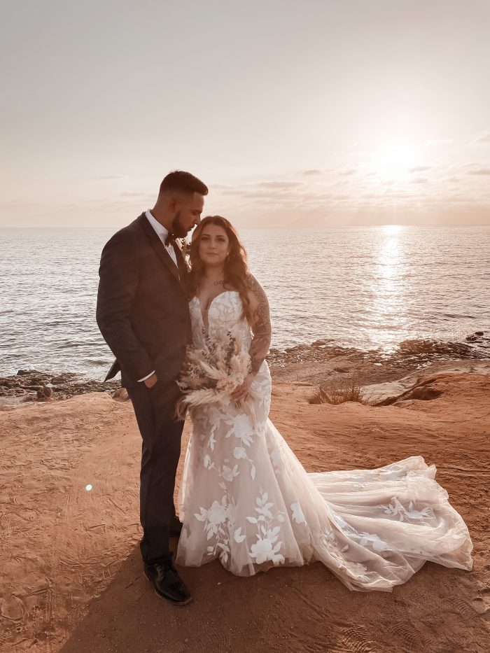 Bride Wearing A Sexy Beach Wedding Dress Called Hattie By Rebecca Ingram In Front Of Ocean Sunset With Groom