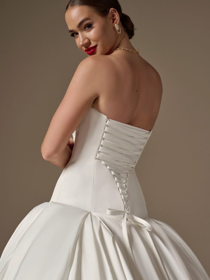 Back view of the Adair wedding dress showing a lace-up corset closure in Leviss stretch satin with a dramatic dropped waist and pleated skirt