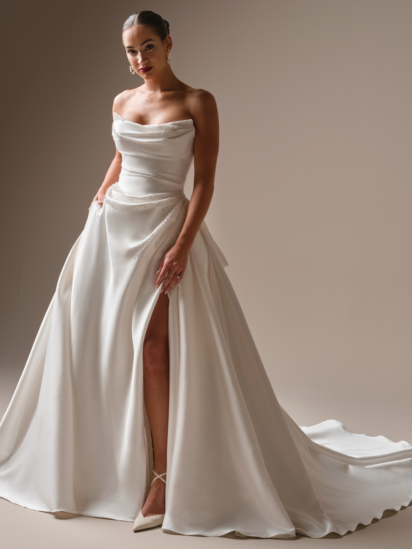 Sottero and Midgley Kincaid ballgown wedding dress featuring a strapless draped satin bodice with subtle beaded detailing, a high slit, and a voluminous skirt for a modern, red-carpet bridal look