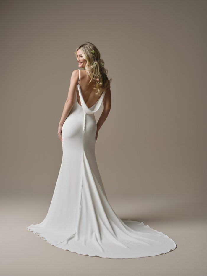 Back view of the Rebecca Ingram Brenda sheath wedding dress featuring a low draped back, delicate spaghetti straps, covered buttons, and a sleek train.
