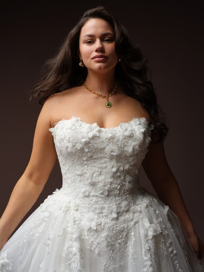 Close-up of the Maggie Sottero Benton ballgown wedding dress featuring a strapless scoop neckline, structured bodice, dimensional floral appliqués, and layered lace detailing.