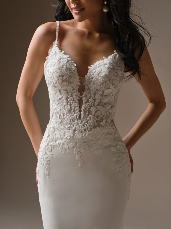 Close-up of an ivory wedding dress featuring a plunging V-neckline with illusion detail, floral lace appliqués, and delicate beaded straps.